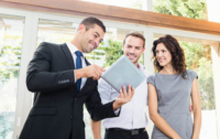 A real estate agent shows two clients listing information on a tablet