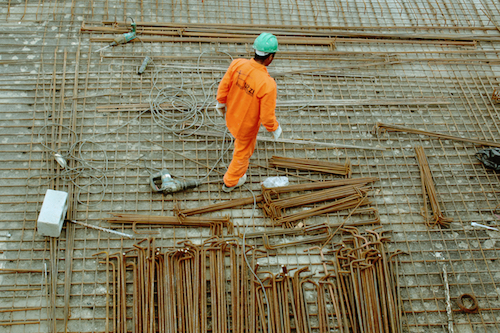 A construction worker in a green helmet and orange jumpsuit on the worksite.